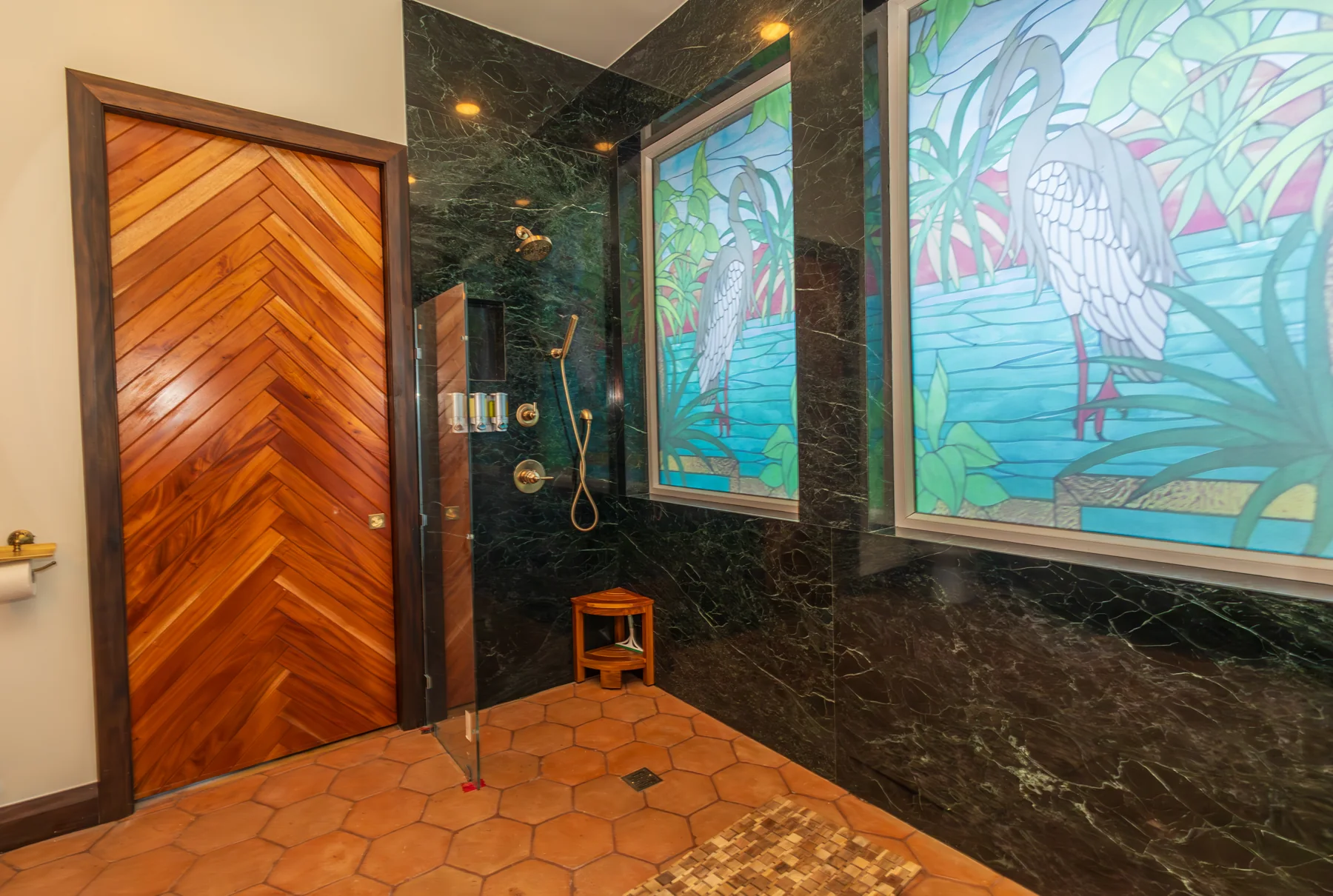 Green stone shower walls and colorful window in the shared bathroom