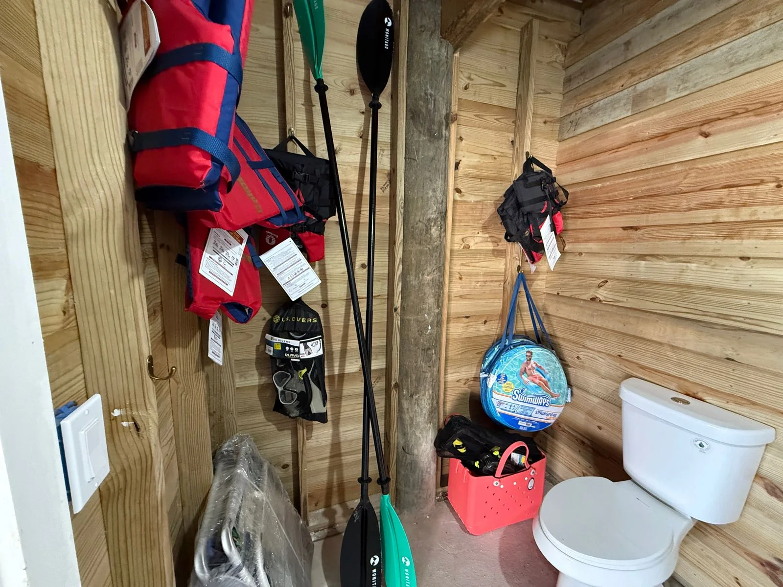 Utility bathroom with toilet, paddles, life jackets, and stored beach gear